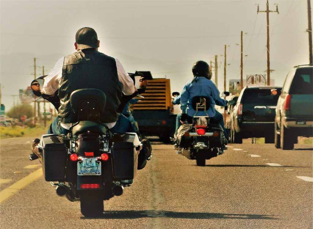 two bikers riding on the highway surrounded by cars in the desert