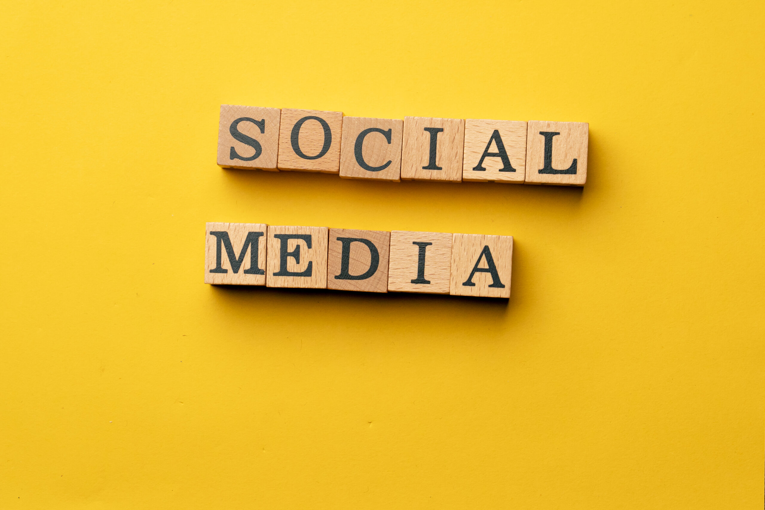 A clear glass hourglass with black sand flowing from the top bulb to the bottom, placed on a small black pedestal against a bright yellow background.