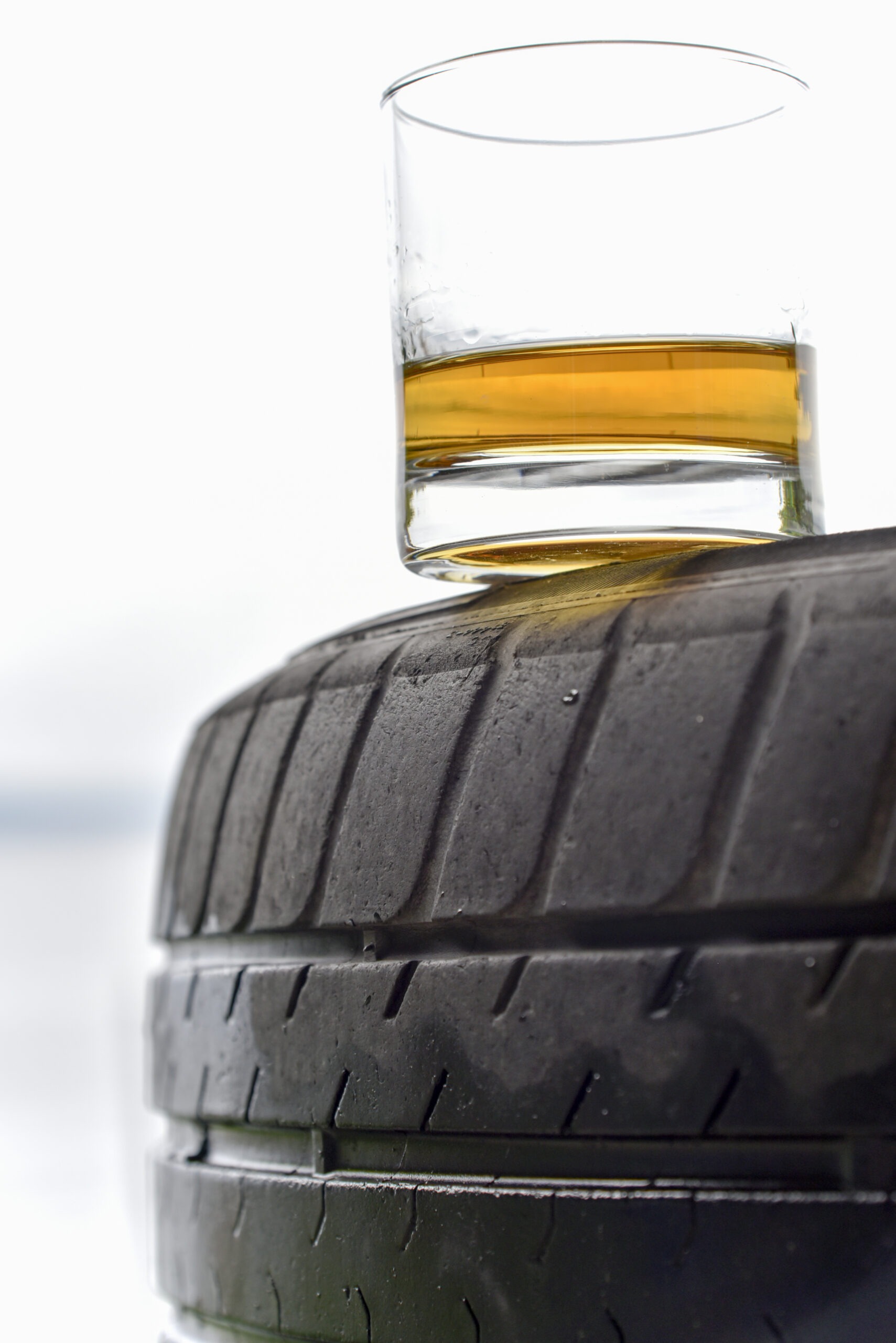whiskey-on-a-turned-over-tire A clear glass hourglass with black sand flowing from the top bulb to the bottom, placed on a small black pedestal against a bright yellow background.